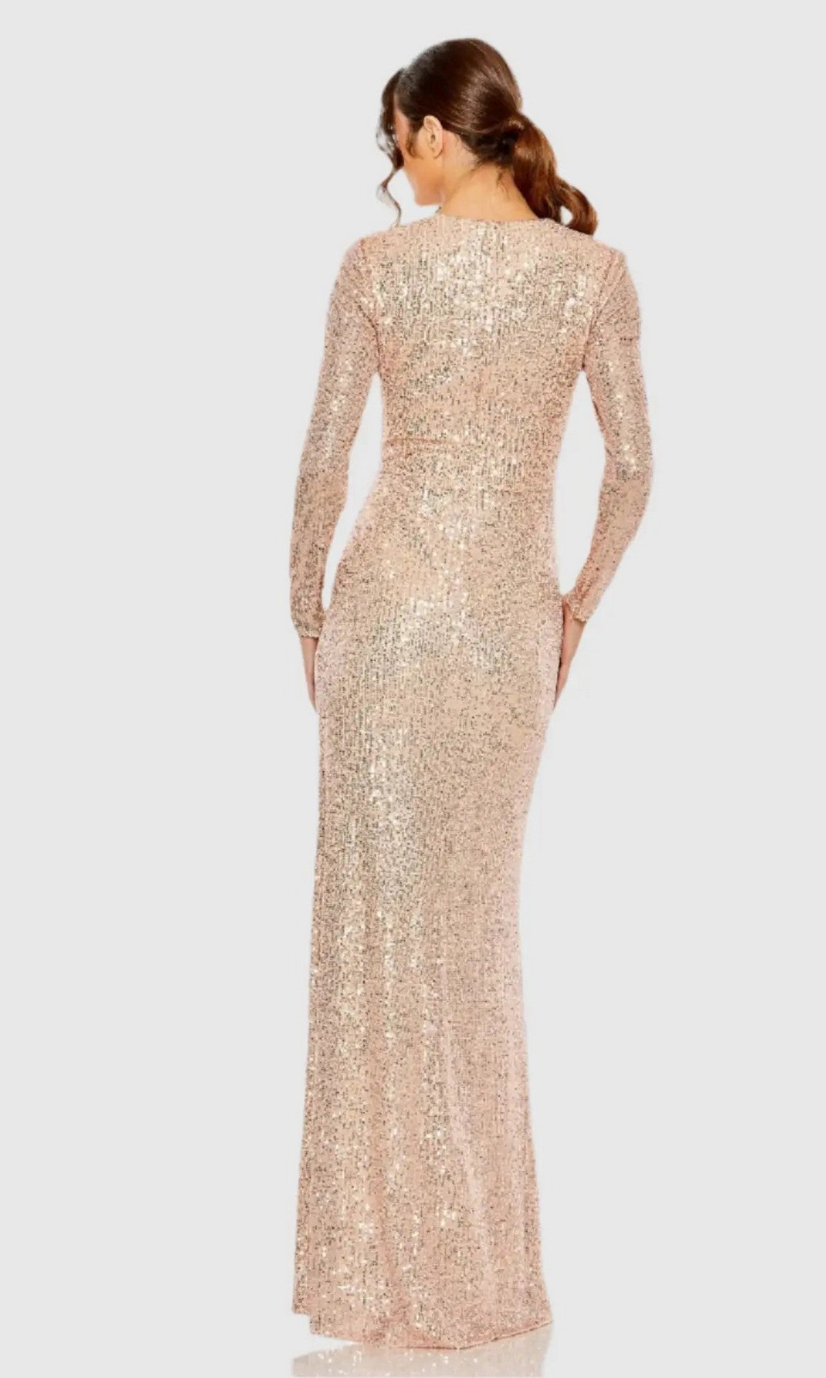 A woman with brown hair in a low ponytail models the Mac Duggal 11659 Long Sleeve Sequin Formal Dress, a rose gold floor-length evening gown that shimmers as she poses from the back against a plain light background.